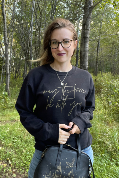 Star Wars sweatshirt May the Force be with you unisex men women shirt sweater top cotton gold scripty cursive galaxy's edge disneyland hollywood studios disneyworld gift woman wearing may the force be with you sweater top with disney crossbody bag and glasses and necklace black with gold scripty font calligraphy