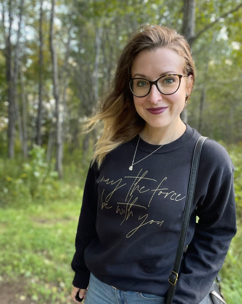 Star Wars sweatshirt May the Force be with you unisex men women shirt sweater top cotton gold scripty cursive galaxy's edge disneyland hollywood studios disneyworld gift woman wearing may the force be with you sweater top with disney crossbody bag and glasses and necklace black with gold scripty font calligraphy