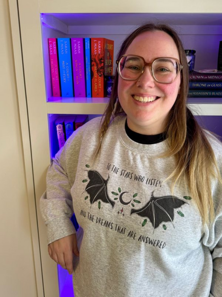 to the stars who listen and the dreams that are answered a court of mist and fury book quote sarah j maas acotar series rhysand feyre archeron night court high lord high lady bat boy t-shirt shirt graphic tee birthday party gift cosplay book club ideas sweatshirt sweater jumper pullover hoodie long sleeve shirt woman in home library living room wearing sweatshirt and glasses reading fangirl book club