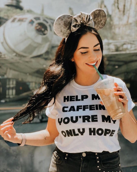 Woman wearing Star Wars Shirt help me caffeine you're my only hope shirt in White with black design. Grey velvet mickey mouse ears in front of the Millennium Falcon holding a Starbucks iced coffee black tap crew. Princess Leia Organa Obi-Wan Kenobi quote the originals movie. coffee, soda, caffeinated, funny, Galaxy's Edge Batuu Disneyland Walt Disney World may the 4th be with you star wars nite celebration convention