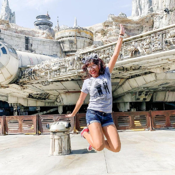 Woman wearing Chewie We're Home Shirt Disney Parks graphic tee Disneyland Disney WORLD Chewbacca holding a Mickey balloon with red heart and Han Solo wearing Mickey ears holding a blaster Neon 90's effect design font