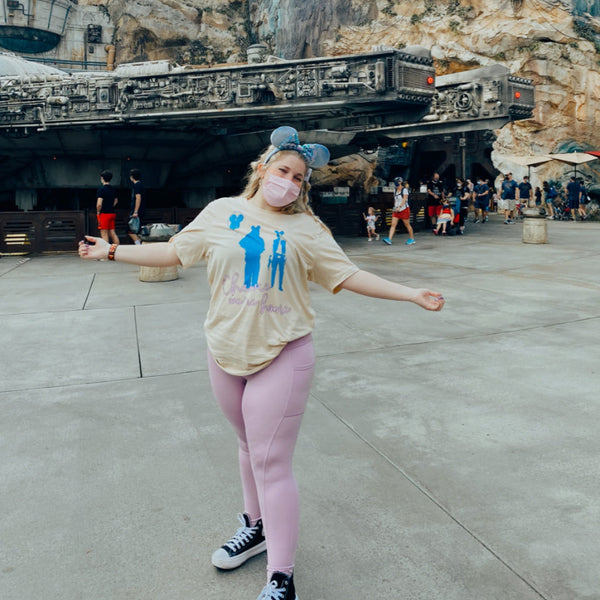 Mask wearing woman wearing a Chewie We're Home Shirt Disney Parks graphic tee Disneyland Disney WORLD Chewbacca holding a Mickey balloon with red heart and Han Solo wearing Mickey ears holding a blaster Neon 90's effect design font
