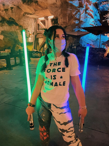 Woman wearing The Force Is female Shirt Star Wars fan holding Ahsoka Tano dual lightsabers and a mask at Galaxy's Edge Batuu at Walt Disney World, Florida.
