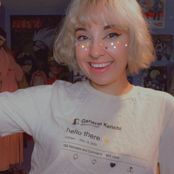 Woman with short blonde hair and bangs wearing General Kenobi Hello There tweet shirt with wave hey hello hand emoji. Prequels Easter eggs, may 19 2005, attack of the clones, general grievous, so uncivilized Obi Wan movie quotes. Available in Sand Beige and Black, size inclusive XS-4XL. Worldwide shipping. Face star stickers