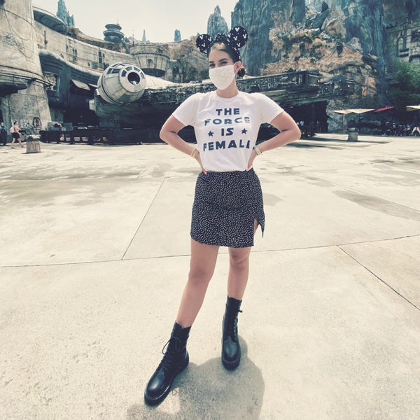 Woman wearing The Force Is Female Shirt with 2 stars in white with black leopard polka dot skirt and black combat boots with black and white Mickey Mouse Ears in front of the Millennium Falcon at Galaxy's Edge, Batuu, in Orlando, Florida at Hollywood Studios, Walt Disney World.