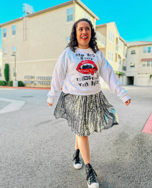 Woman wearing white Red Lip Classic vampire lips Halloween sweatshirt with metallic silver pleated skirt and black high-top sneakers, styled for casual streetwear look. taylor swift 1989 style