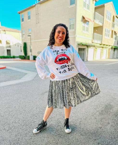 Woman wearing white Red Lip Classic vampire lips Halloween sweatshirt with metallic silver pleated skirt and black high-top sneakers, styled for casual streetwear look. taylor swift 1989 style