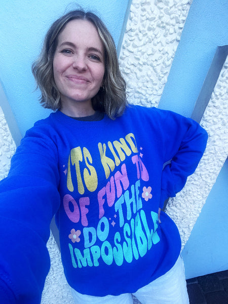 Woman wearing Walt Disney Quote Sweatshirt Is Kind Of Fun To Do The Impossible in Blue with Hippie Flowers and Stars Disney Parks Outfit Small World Wall Disneyland Theme Park