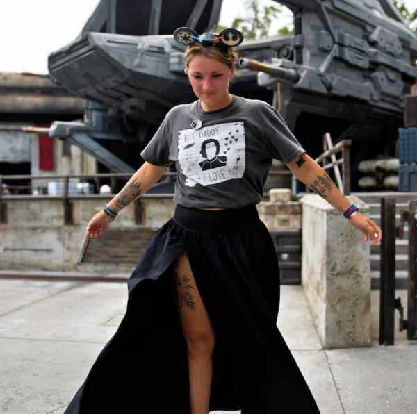 Woman at Galaxy's Edge Batuu Disneyland Theme Park wearing But Daddy I Love Him Kylo Ren Comfort Colors Shirt in grey with black and white design and Star Wars mickey ears with black skirt and tattoos