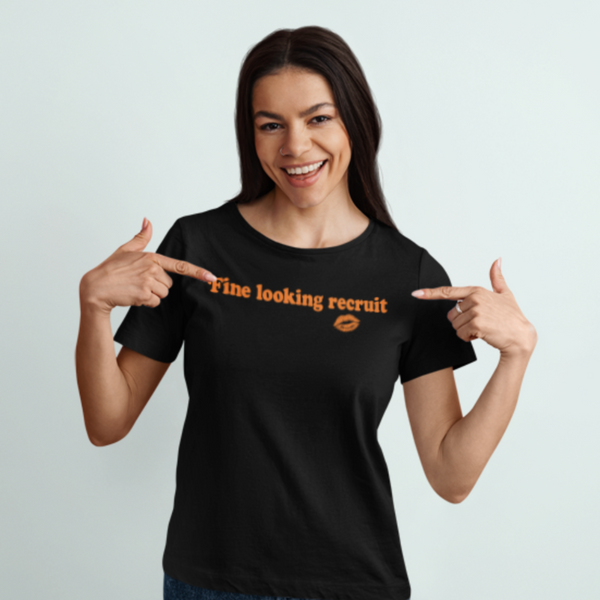 Woman wearing a black unisex graphic t-shirt with distressed orange text reading “Fine Looking Recruit” and a small orange kiss graphic. rise of the resistance shirt