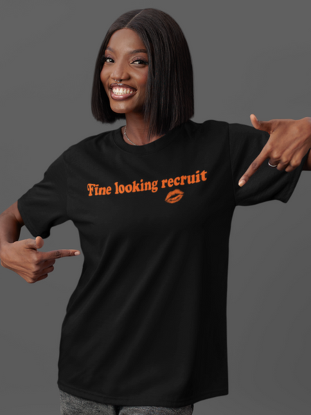 Woman wearing a black unisex graphic t-shirt with distressed orange text reading “Fine Looking Recruit” and a small orange kiss graphic. rise of the resistance shirt
