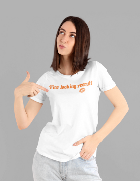 Woman wearing a white unisex graphic t-shirt with distressed orange text reading “Fine Looking Recruit” and a small orange kiss graphic. rise of the resistance shirt