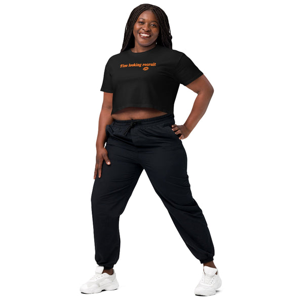 Woman wearing a black unisex graphic t-shirt with distressed orange text reading “Fine Looking Recruit” and a small orange kiss graphic.