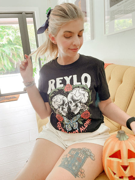 Black t-shirt with skull design and text on a white background Reylo Halloween shirt graphic tee kylo ren rey skulls skeletons you're not alone neither are you star wars woman wearing with black bow and pumpkin dr who tattoo halloween