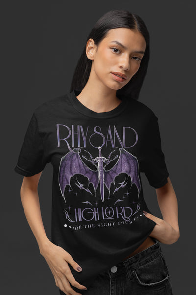 Woman wearing Rhysand High Lord Shirt on Black Comfort Colors with purple design. Front design says Rhysand High Lord of the Night Court. Back design has ACOTAR inspired references. Bat boys wings sword book reading faerie outfit top.