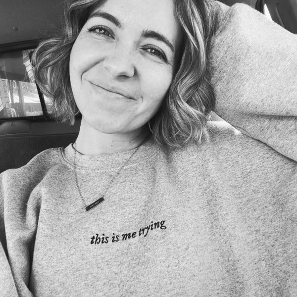 Grey unisex sweatshirt with minimalist black embroidered text reading ‘this is me trying’; folklore-inspired Swiftie aesthetic crewneck. Taylor Swift music lyrics gift outfit