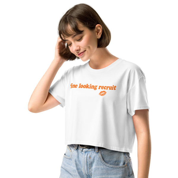 Woman wearing a white unisex graphic t-shirt with distressed orange text reading “Fine Looking Recruit” and a small orange kiss graphic.