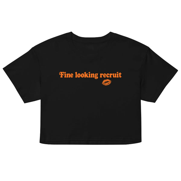 Woman wearing a black unisex graphic t-shirt with distressed orange text reading “Fine Looking Recruit” and a small orange kiss graphic.