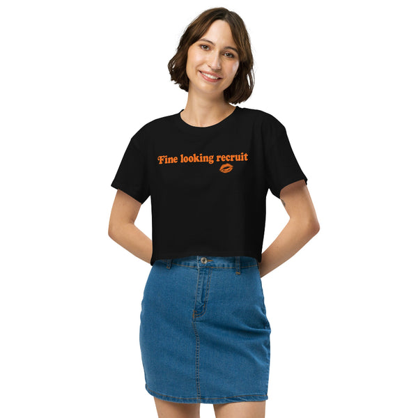 Woman wearing a black unisex graphic t-shirt with distressed orange text reading “Fine Looking Recruit” and a small orange kiss graphic.